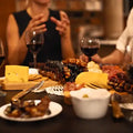 A group of friends sitting around a Charcuterie board that is filled up with Churchkhela and cheese and crackers. They all have glasses of red wine.