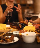 A group of friends sitting around a Charcuterie board that is filled up with Churchkhela and cheese and crackers. They all have glasses of red wine.