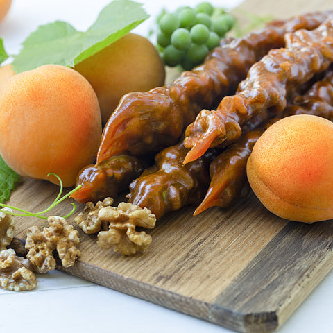 A photo of apricot flavoured Churchkhela on a charcuterie board with walnuts grapes and apricots.