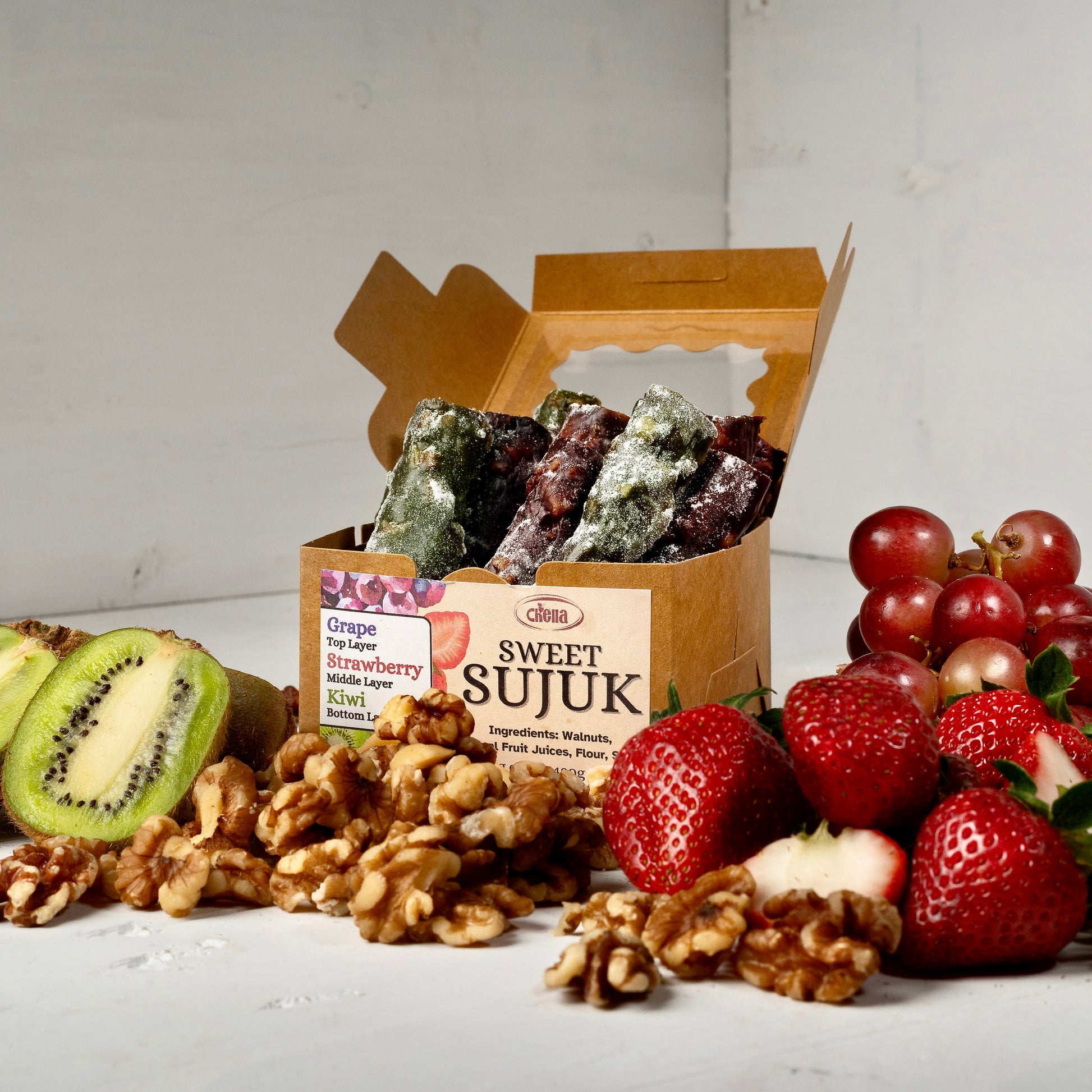 A photo of our Sweet Sujuk in a box with kiwis, walnuts, strawberries and grapes layed out in front of the box, helping to show what flavours we carry.