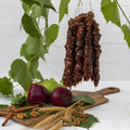 A bundle of Churchkhela hung over a cutting board that has apples, cinnamon, walnuts and wheat stocks displayed on it