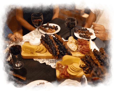 a photo of a couple friends sitting around a charcuterie board with glasses of wine. The charcuterie board is filled with churchkhela and other foods such as cheese, crackers and meats