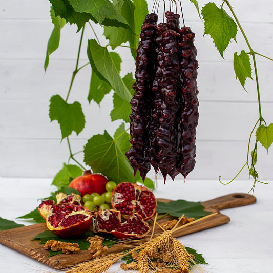 A bundle of Churchkhela hung over a cutting board that has pomegranates, walnuts and wheat stocks displayed on it